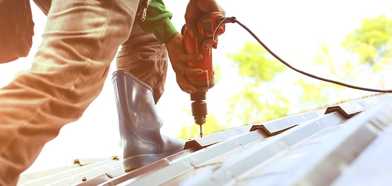 Corded drill  being used to screw metal roof sheets