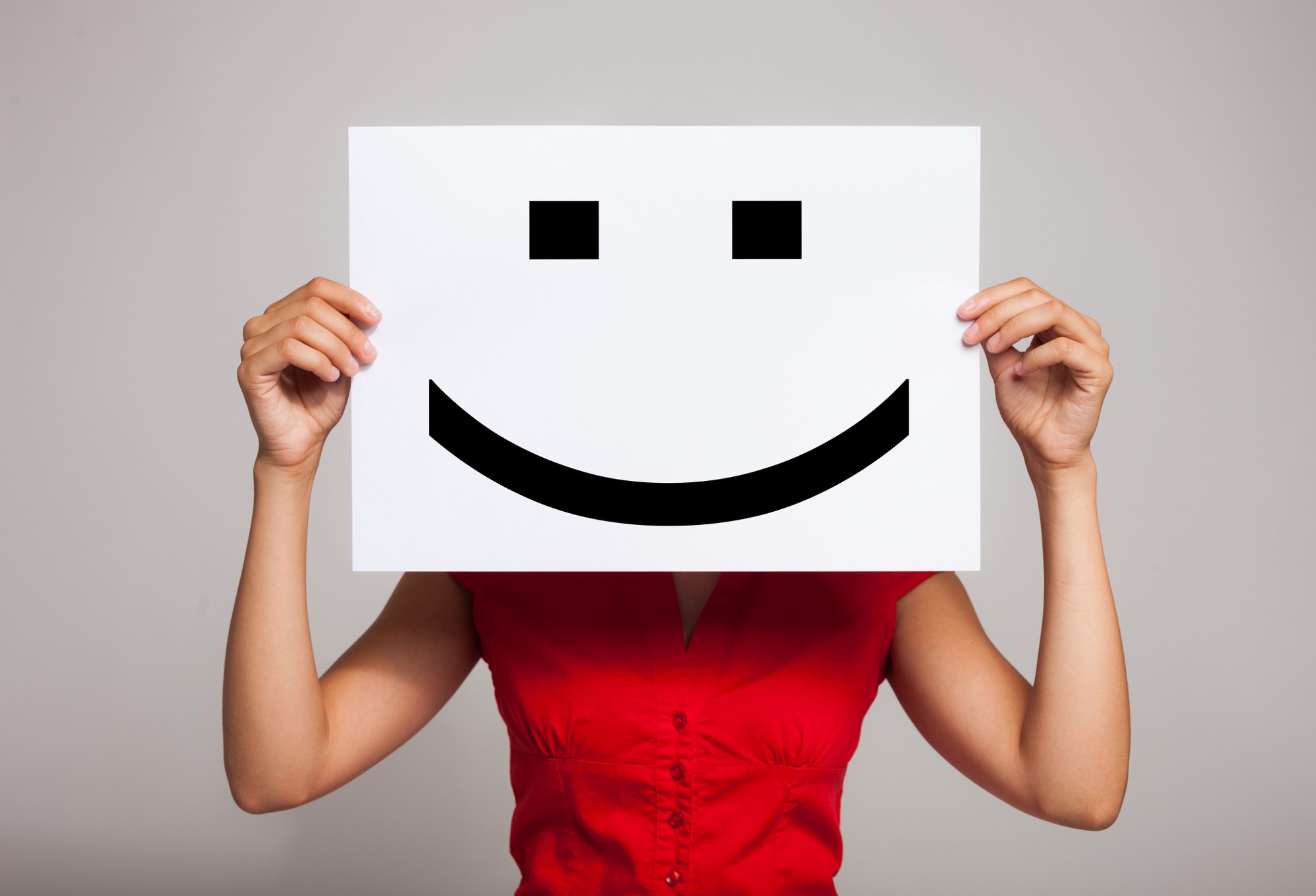 Woman holding placard with smiley face in front of head